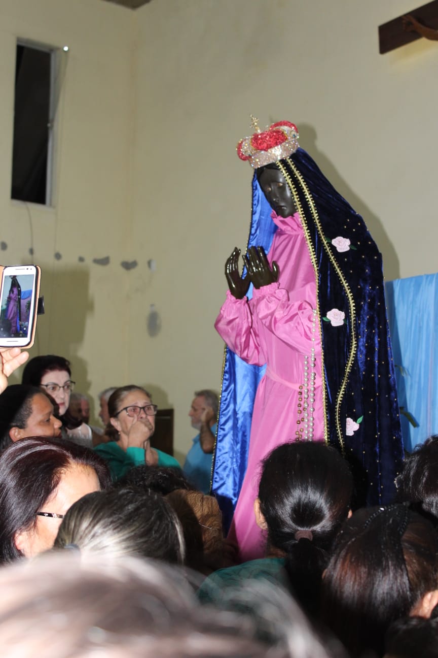 Imagem de Nossa Senhora Aparecida vestida de rosa cercada de fiéis na capela